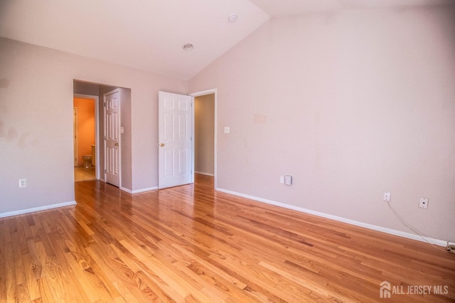 unfurnished bedroom featuring vaulted ceiling, light wood-type flooring, baseboards, and ensuite bath