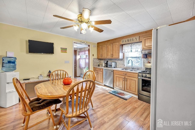 kitchen with appliances with stainless steel finishes, light hardwood / wood-style floors, sink, backsplash, and ceiling fan