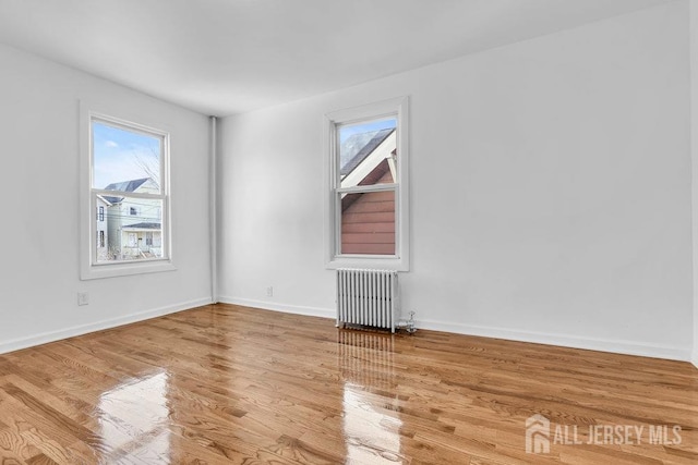 spare room featuring radiator heating unit, a wealth of natural light, and hardwood / wood-style floors