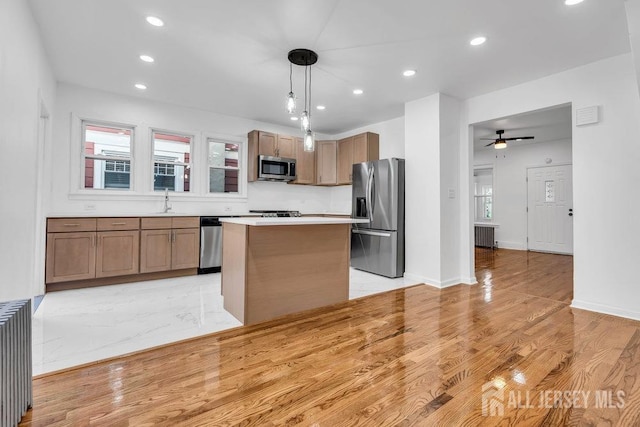 kitchen featuring appliances with stainless steel finishes, hanging light fixtures, radiator heating unit, a kitchen island, and a healthy amount of sunlight