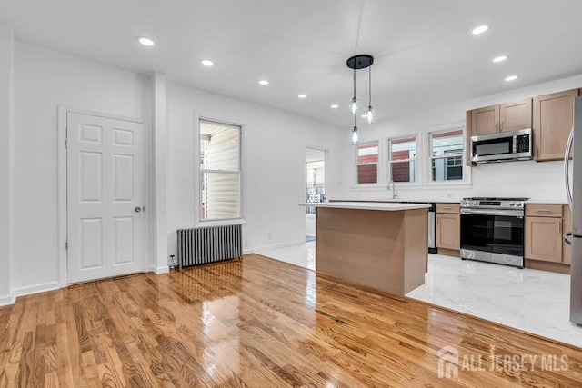 kitchen featuring appliances with stainless steel finishes, radiator heating unit, light wood-type flooring, decorative light fixtures, and sink