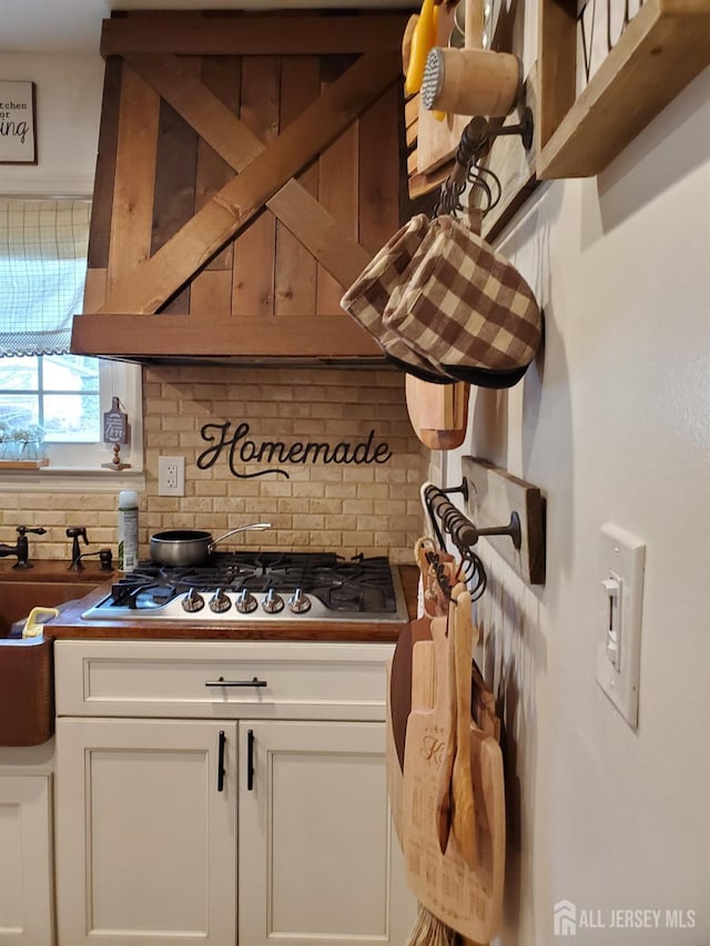 kitchen with tasteful backsplash, stainless steel gas cooktop, white cabinets, and a sink