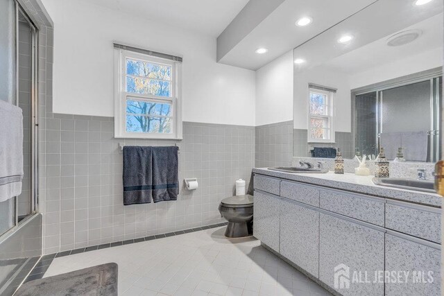 bathroom featuring toilet, a sink, tile walls, and tile patterned floors