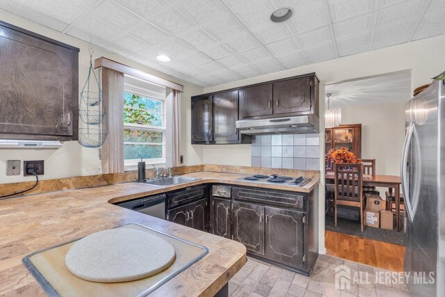 kitchen with light countertops, appliances with stainless steel finishes, a sink, dark brown cabinets, and under cabinet range hood