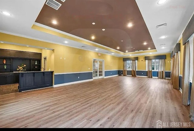 workout room featuring a tray ceiling, light wood-style flooring, crown molding, french doors, and recessed lighting
