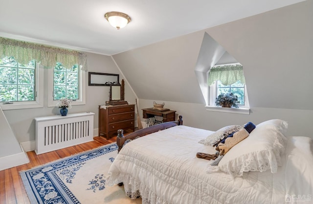 bedroom with vaulted ceiling, radiator heating unit, and hardwood / wood-style flooring