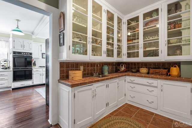 interior space featuring black double oven, white cabinetry, tile counters, pendant lighting, and decorative backsplash