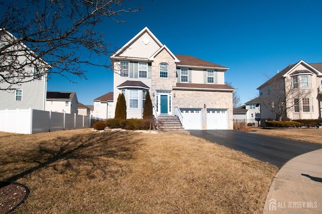 traditional-style house with aphalt driveway, a front lawn, fence, and a garage