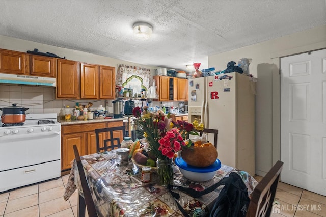 209 New St, New Brunswick, NJ 08901 - kitchen featuring white appliances, under cabinet range hood, brown cabinets, light tile patterned floors, and a textured ceiling
