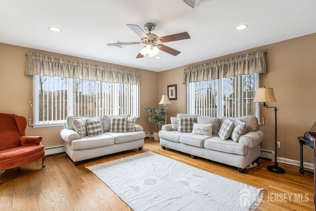 living area with light wood finished floors, a baseboard heating unit, and a ceiling fan