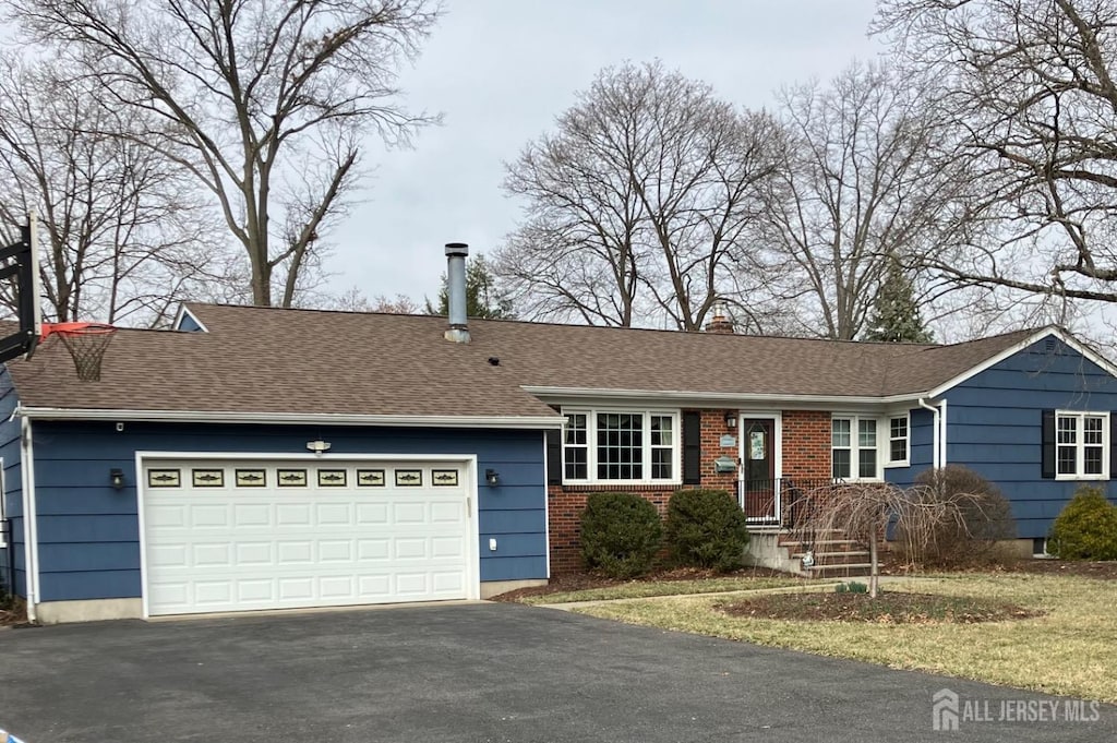 single story home featuring a shingled roof, a garage, driveway, and a chimney