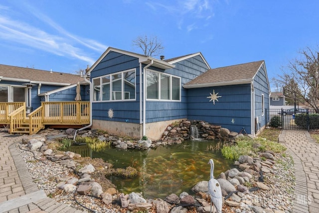 exterior space with a deck, fence, and a small pond