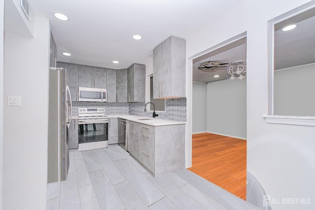 kitchen with appliances with stainless steel finishes, gray cabinetry, light countertops, recessed lighting, and decorative backsplash