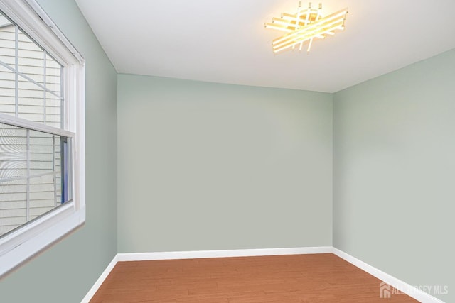 empty room with wood finished floors, a chandelier, and baseboards