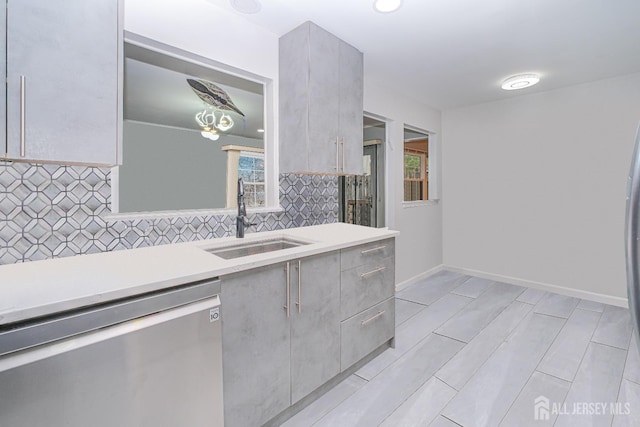 kitchen with dishwasher, a sink, light countertops, and decorative backsplash