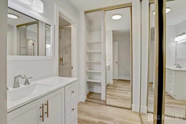 bathroom with two vanities, a stall shower, a sink, wood finished floors, and baseboards