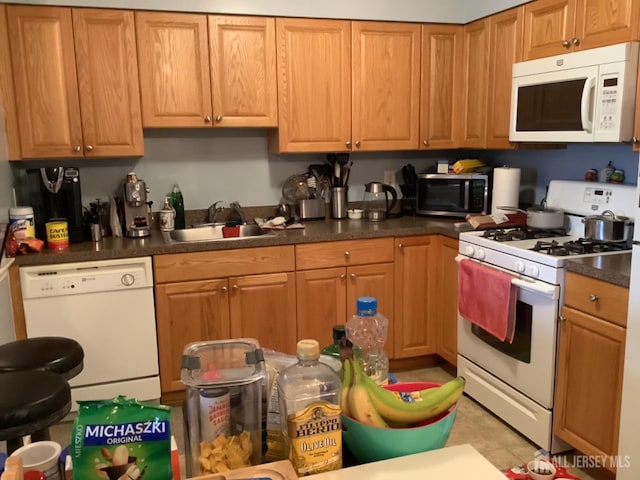 kitchen featuring dark countertops, white appliances, brown cabinets, and a sink