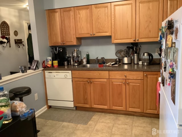 kitchen with dark countertops, white appliances, brown cabinets, and a sink