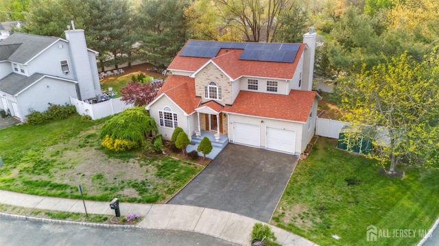 view of front facade featuring fence, a garage, a front yard, roof mounted solar panels, and driveway