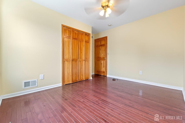 unfurnished bedroom with visible vents, a closet, dark wood-style flooring, baseboards, and a ceiling fan