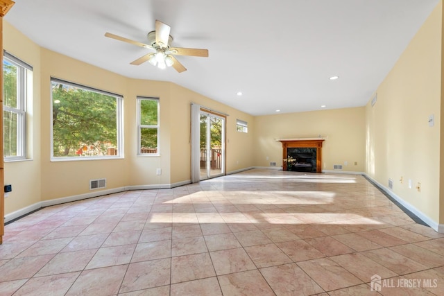 unfurnished living room featuring visible vents, plenty of natural light, a fireplace, and ceiling fan
