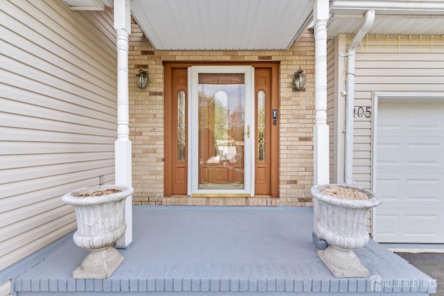 entrance to property with brick siding, a garage, and covered porch