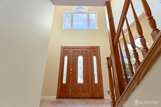 entryway with stairs, baseboards, visible vents, and a high ceiling