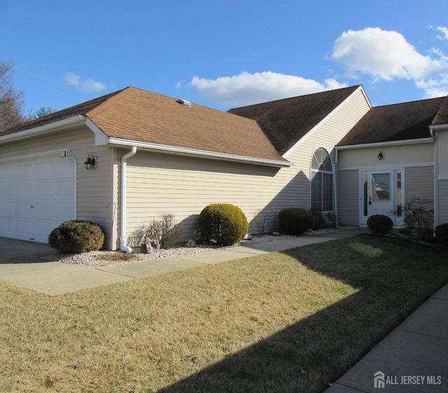 view of side of property featuring roof with shingles, a lawn, and a garage