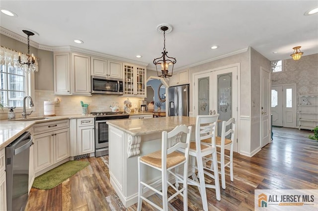 kitchen featuring stainless steel appliances, a chandelier, a sink, wood finished floors, and cream cabinetry