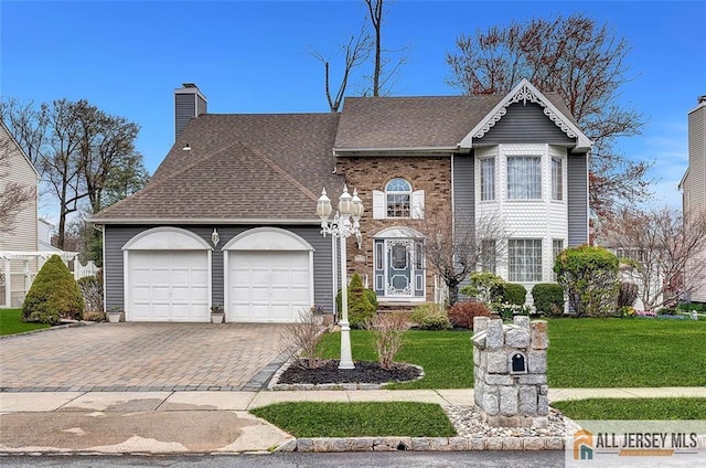 view of front facade with an attached garage, decorative driveway, a shingled roof, a front lawn, and a chimney