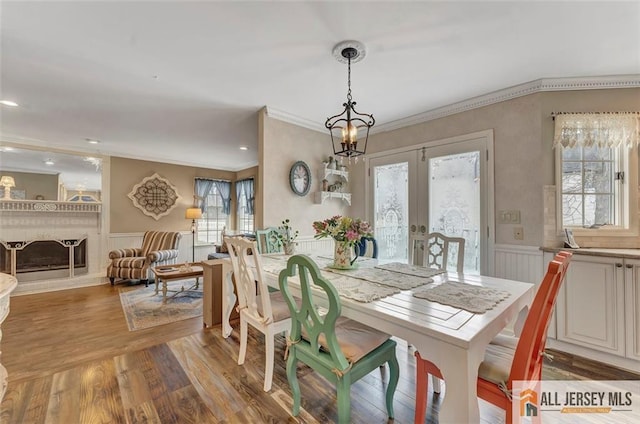 dining space featuring crown molding, a wainscoted wall, light wood-style flooring, french doors, and a decorative wall