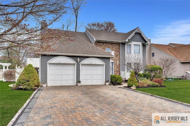 traditional home featuring decorative driveway, an attached garage, a front yard, a chimney, and roof with shingles