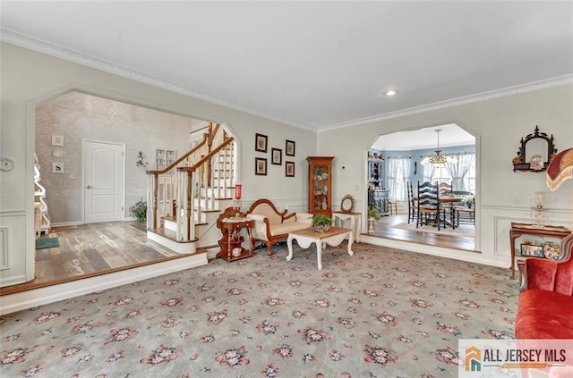 living area featuring arched walkways, crown molding, stairs, and a chandelier