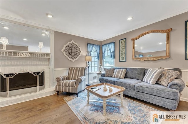 living area with wainscoting, crown molding, wood finished floors, a brick fireplace, and recessed lighting