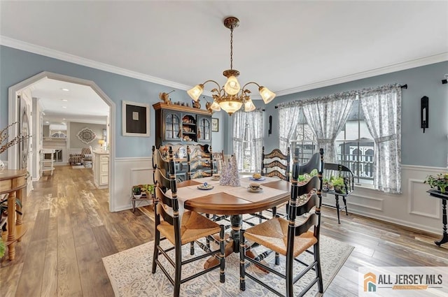dining area featuring a chandelier, arched walkways, a wainscoted wall, ornamental molding, and wood finished floors