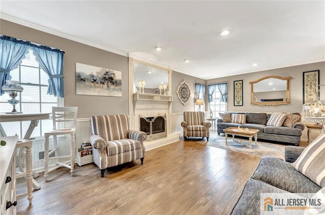 living area with ornamental molding, hardwood / wood-style floors, wainscoting, a large fireplace, and recessed lighting