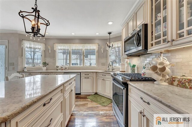 kitchen with appliances with stainless steel finishes, a chandelier, cream cabinetry, a sink, and light wood-type flooring