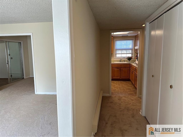 corridor featuring sink, a textured ceiling, light carpet, and a baseboard heating unit