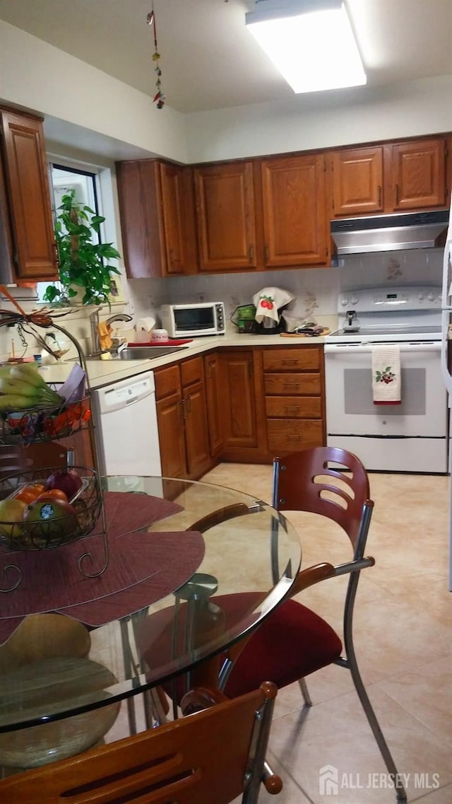 kitchen featuring brown cabinetry, white appliances, light countertops, and under cabinet range hood