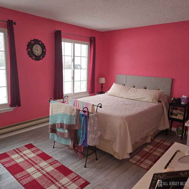 bedroom with wood-type flooring, a textured ceiling, and a baseboard heating unit