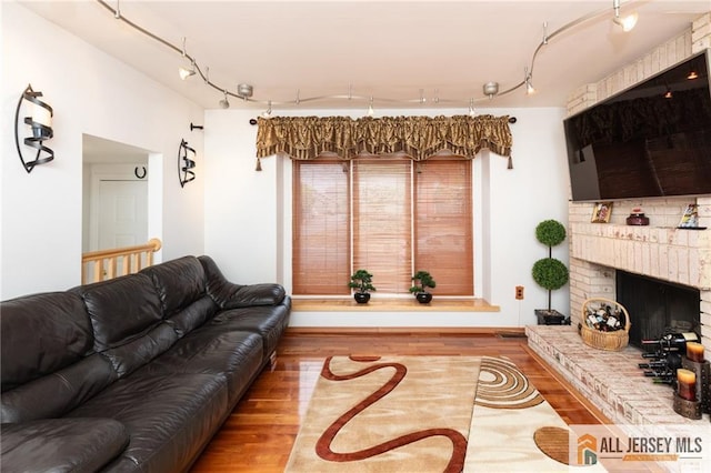 living area featuring track lighting, a brick fireplace, and wood finished floors