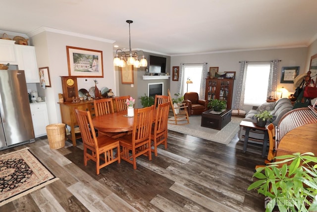 dining space with a fireplace, crown molding, a notable chandelier, and wood finished floors