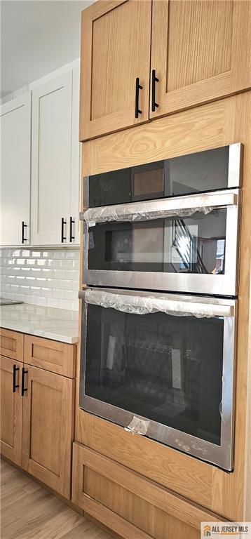 kitchen view of stainless steel oven, light countertops, light wood-style flooring, decorative backsplash, and white cabinetry