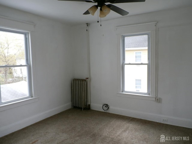 carpeted empty room with baseboards, ceiling fan, plenty of natural light, and radiator heating unit