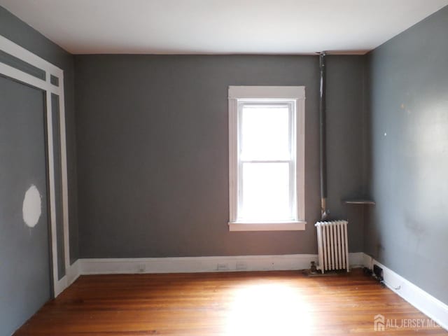 spare room featuring baseboards, wood finished floors, and radiator