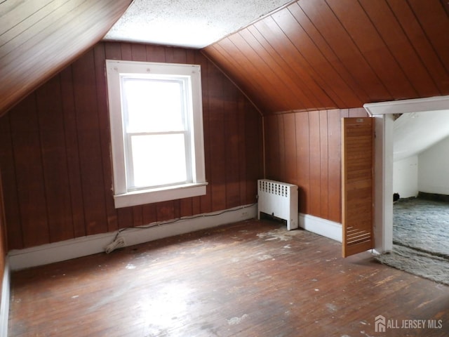 bonus room featuring radiator, wood walls, hardwood / wood-style flooring, and lofted ceiling
