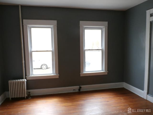 unfurnished room featuring wood finished floors, baseboards, and radiator heating unit