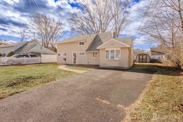 view of front of home featuring driveway, a lawn, an outbuilding, fence, and a storage unit