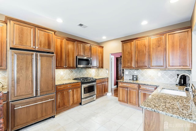 kitchen with light stone counters, a sink, visible vents, appliances with stainless steel finishes, and tasteful backsplash