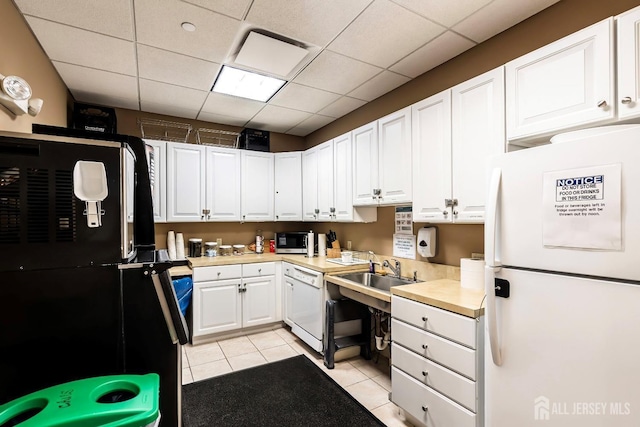 kitchen with white appliances, light tile patterned floors, white cabinets, a drop ceiling, and light countertops